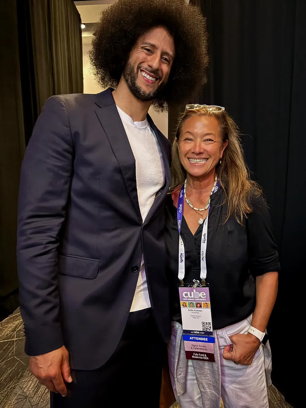 Scilla, smiling and wearing a CUBE conference badge, stands backstage beside Colin Kaepernick.