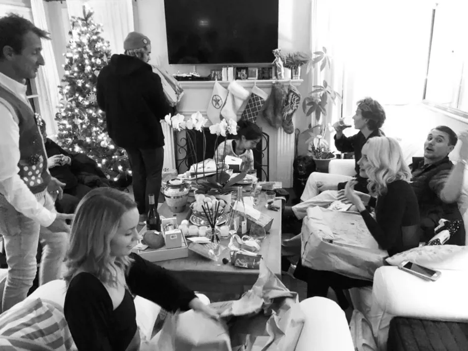 Black-and-white photo of the family gathered around a coffee table of presents in a living room, Christmas tree and stockings behind them.