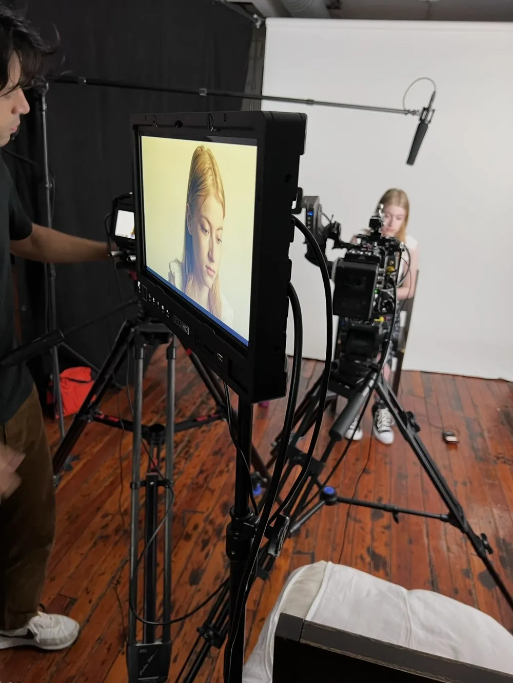 A film set: a monitor shows a young woman being interviewed, with the camera, boom mic and crew around her.