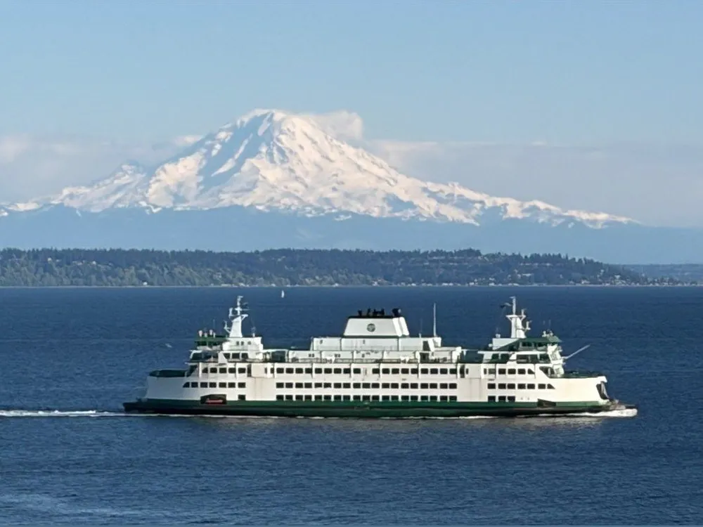 A green-and-white ferry crossing blue water, with snow-capped Mount Rainier rising behind the shoreline.