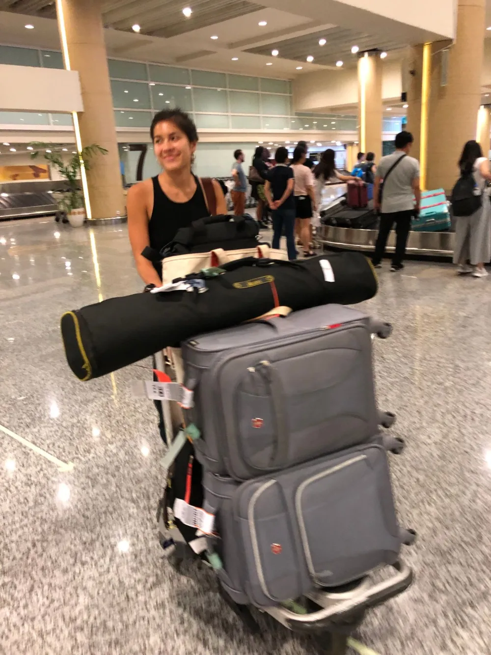 Natalie smiling behind an airport trolley piled high with camera cases and luggage.