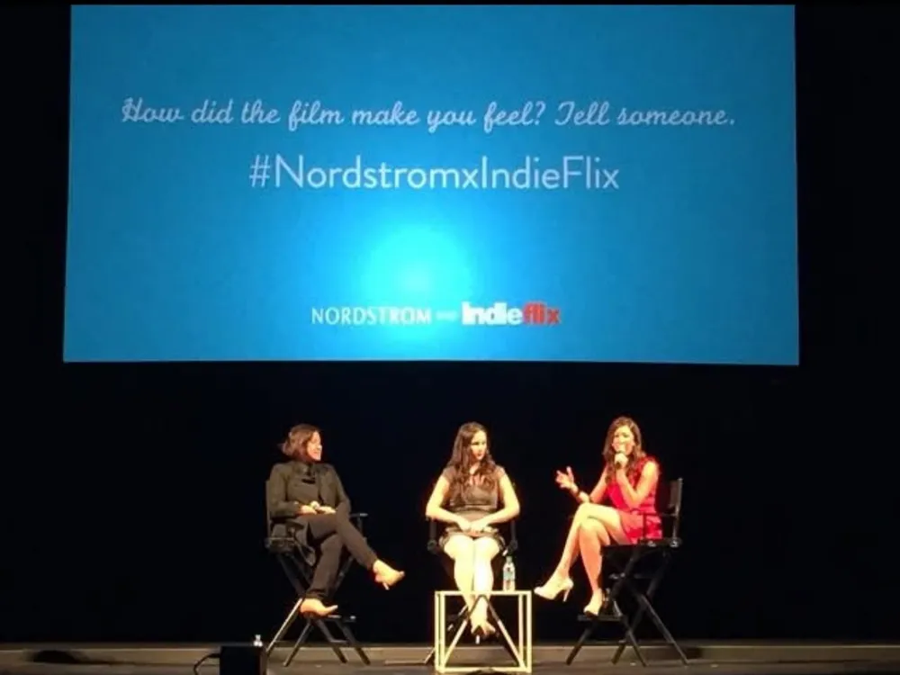 Three women in director’s chairs on a dark stage, beneath a screen reading “How did the film make you feel? Tell someone. #NordstromxIndieFlix”.