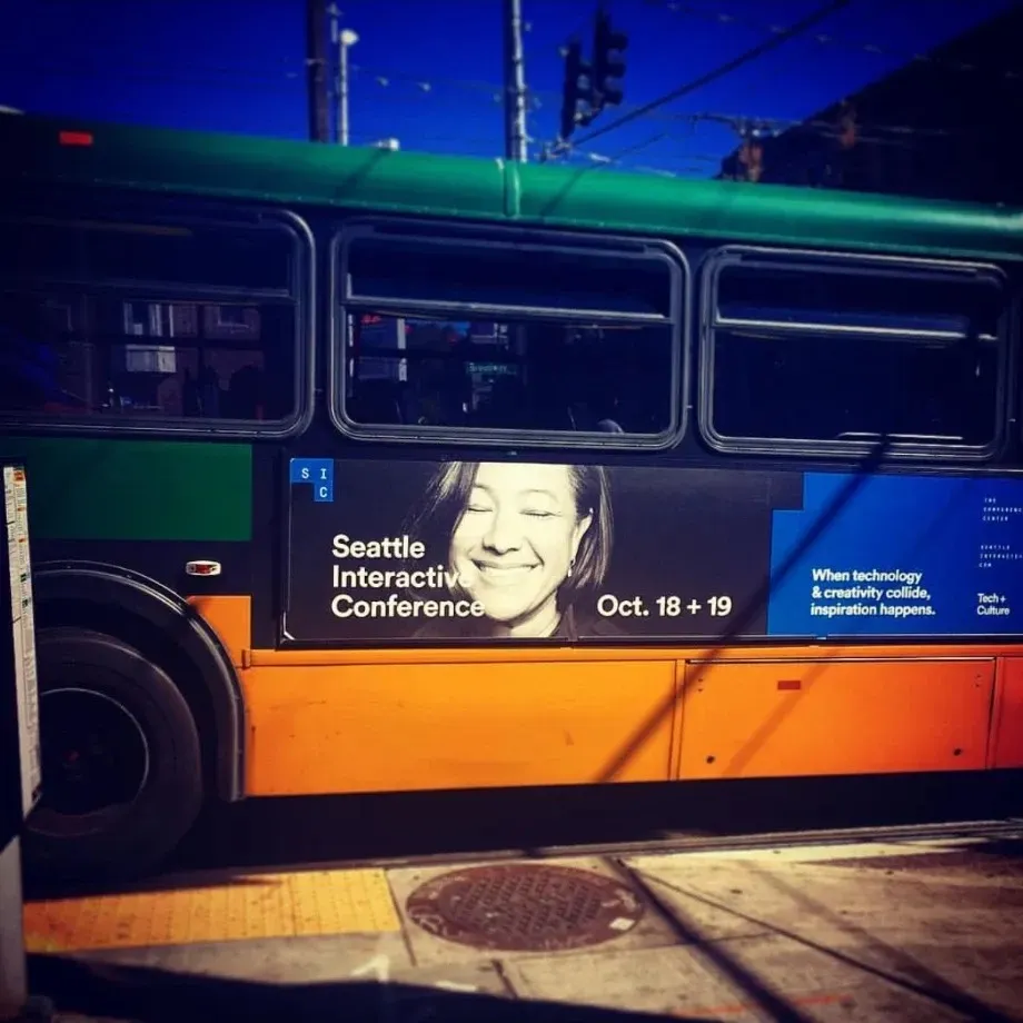 A Seattle city bus with a side ad for the Seattle Interactive Conference, Oct. 18 + 19, featuring a smiling black-and-white photo of Scilla.
