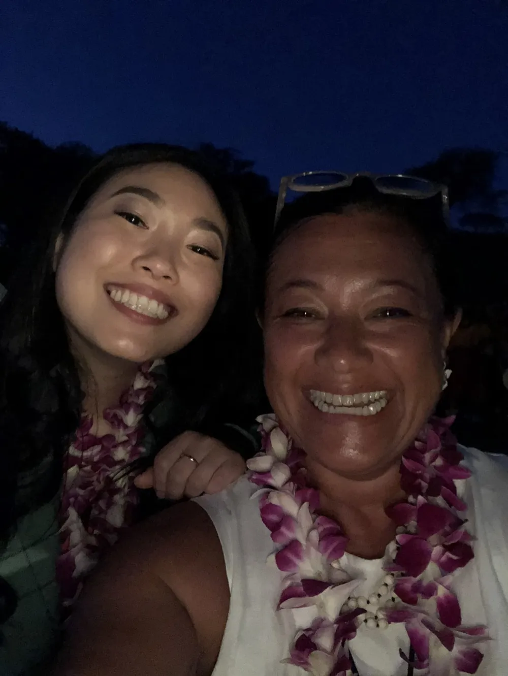 A night-time selfie of Scilla and Awkwafina, both laughing and wearing purple and white leis.