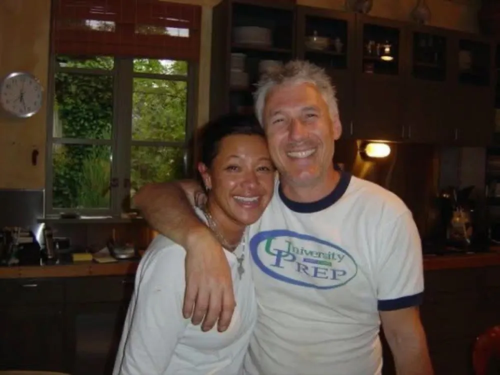 Scilla and Carlo Scandiuzzi, arms around each other and laughing, in a kitchen.