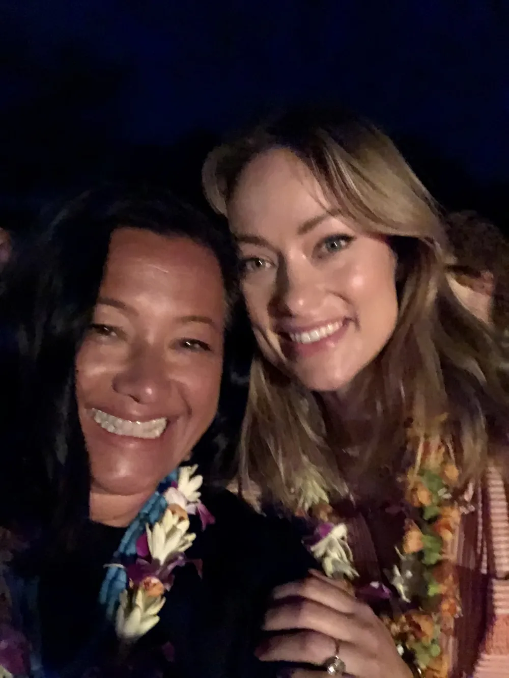 A night-time selfie of Scilla and Olivia Wilde, both smiling and wearing leis.