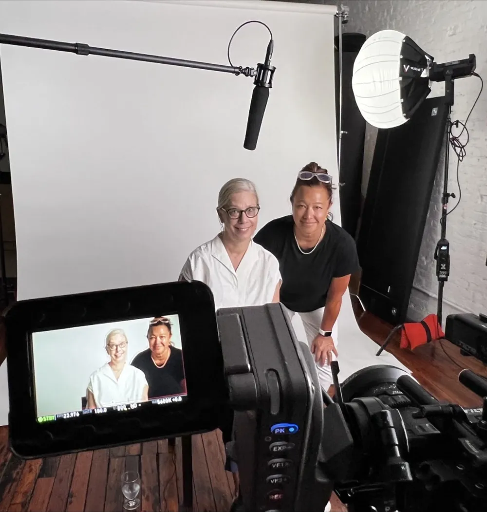 Scilla and her friend JC pose in front of a white backdrop, both shown on the camera monitor in the foreground.